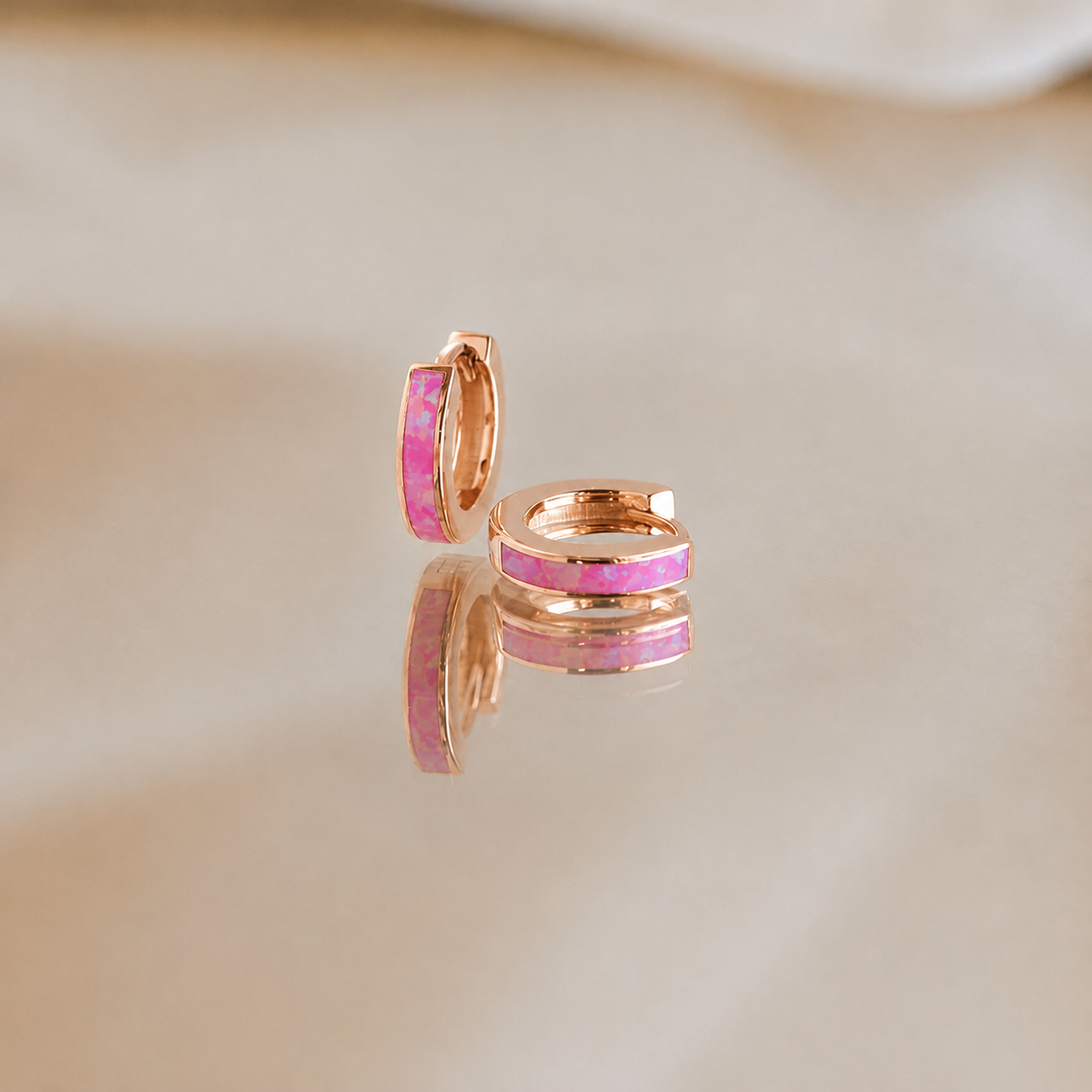 Rose gold hoop earrings with pink enamel accents on a beige background